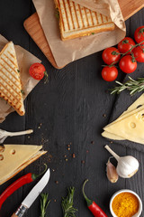 Appetizing sandwiches with tomato cheese and herbs with ingredients on a black wooden table