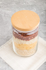 glass jar with different kinds of rice poured in layers on a gray concrete background. side view, close up.