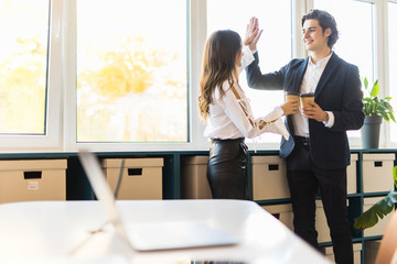 Sharing fresh news. Two joyful young people in formalwear holding cups of coffee and discussing something while working together
