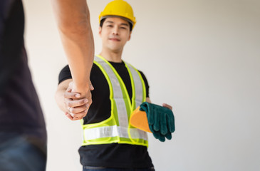 Engineers in protective helmets and vests are shaking hands while working in successful projects, Unity and teamwork concept..