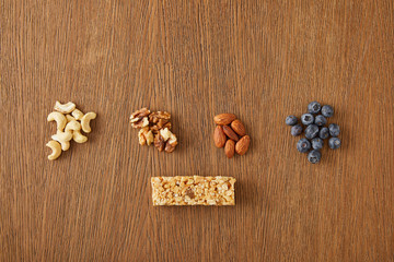 Fototapeta na wymiar Top view of walnuts, almonds, cashews, blueberries and cereal bar on wooden background