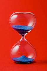 Crystal hourglass on a red background, the concept of passing time.