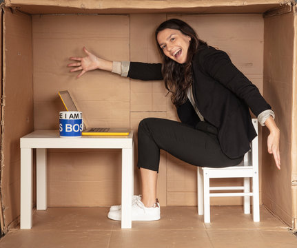young beautiful businesswoman sitting in an office cardboard box, shows her workplace