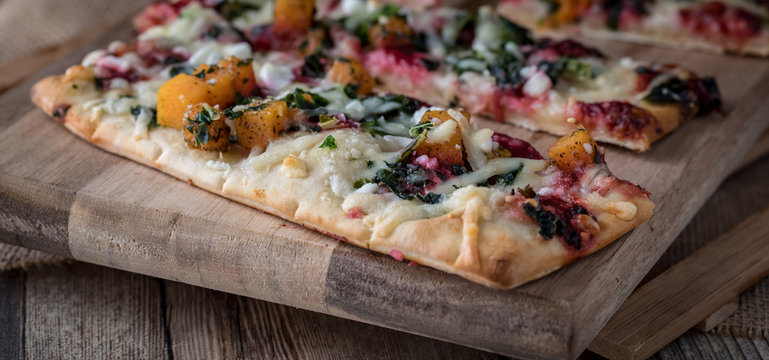 A close up view of slices of root vegetable flat bread pizza ready for eating.