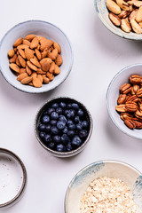 Ingredients for homemade granola: oatmeal, pecans, almond, brazilan nuts, blueberries in a bowls on grey background. Healthy diet breakfast. Flatlay. Top view. Selective focus