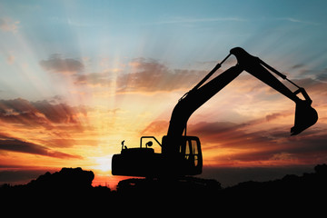 Excavators are digging the soil in the construction site on the sunset background,With image silhouette backhoe