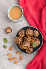 Chocolate caramel ball candies with almonds and a cup of coffee on a gray concrete background and red textile. top view, close up.