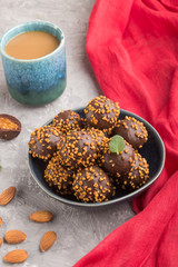 Chocolate caramel ball candies with almonds and a cup of coffee on a gray concrete background and red textile. Side view.