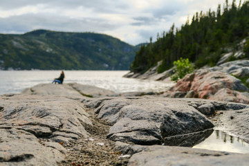 Fototapeta na wymiar Rock shore at the entrance of Saguenay fjord view from Tadoussac with a blurry happy woman in the background