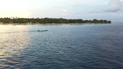 Drone view of sea coast with greenery and floating boat on waves to transport passengers between the islands. Aerial drone view of sunset over sea, drone flies close to ocean in asia. - Powered by Adobe