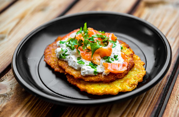 potato pancakes withsalmon fish and sour cream in a plate on wooden table