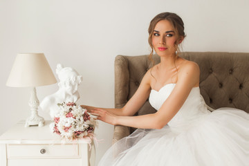 Young bride in a beautiful dress sitting at home with nice white interior. Wedding concept.