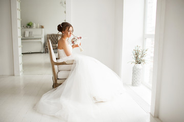 Naklejka premium Young bride in a luxury dress holding a bouquet of flowers in bright white studio. Wedding fashion concept.