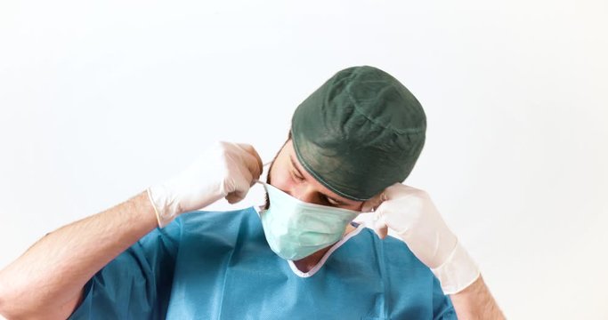 Primo piano di un giovane uomo medico, si toglie la mascherina e fa un bel sorriso di fronte la telecamera. Sfondo bianco.
