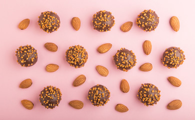 Chocolate caramel ball candies with almonds in a row on a pastel pink background. top view.