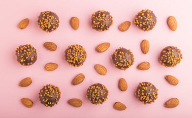 Chocolate caramel ball candies with almonds in a row on a pastel pink background. top view.