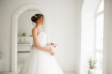 Young bride in a luxury dress holding a bouquet of flowers in bright white studio. Wedding fashion concept.