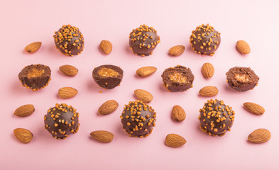 Chocolate caramel ball candies with almonds in a row on a pastel pink background. side view.