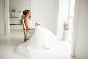 Young bride in a luxury dress holding a bouquet of flowers in bright white studio. Wedding fashion concept.