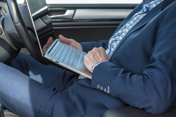 Businessman in the blue suit working in the car typing laptop on the knees