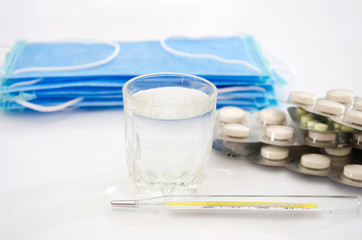 pills in blister packs glass of water, thermometer and medical mask on white. Health concept.