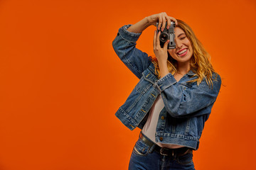 Smiling woman  in a jeans jacket with fair wavy hair takes a photo on old photo camera.