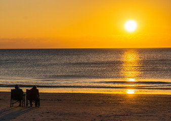two people sitting on beach enjoying the sunset 