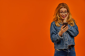 Fototapeta na wymiar Happy woman with wavy hair in a denim jacket with wired headphones holds a phone in her right hand.