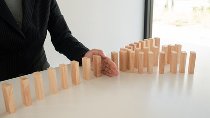 Businessman hand Stopping falling dominos in a business crisis. lost small to protect the rest, managing risk by exiting losing business management, develop business strategy