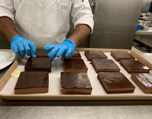 Cook is preparing many chocolate cakes. He is wearing blue gloves. It is a galley on a cruise ship....