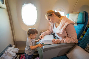 a young beautiful mother sits in an airplane chair and reads a book to her little cute toddler, who is standing in front of her. close-up, soft focus, top view.  place for copyspace, empty page