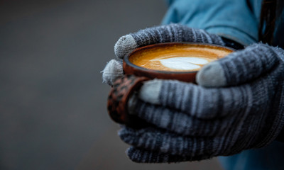 female hands in gloves hold a cup of hot cappuccino coffee on the street