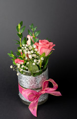Small vase with pink bow and rose flowers, black background with copy space