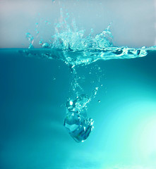 An ice cube falling into the water with a splash and water bubbles under water.