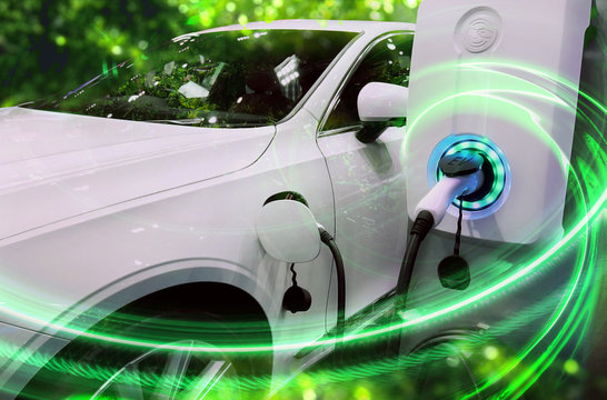 EV Car Or Electric Vehicle At Charging Station With The Power Cable Supply Plugged In On Blurred Nature With Green Energy Power Effect. Eco-friendly Sustainable Energy Concept.