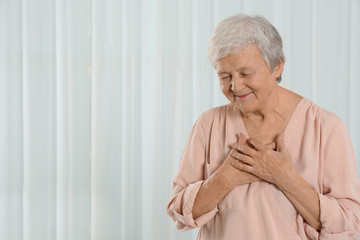 Grateful senior woman with hands on chest against light background. Space for text