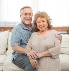 Portrait of elderly senior asian couple happy together at home.Elder man arm hug elder woman shoulder look at camera.