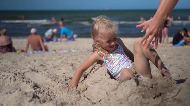 girl buried in sand break free and have fun with mother. Blurred people and sea