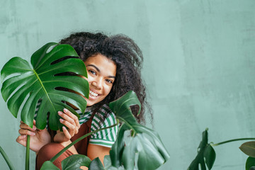 Young woman with natural make up and tropical monstera leaf in hand over green background with copy space. Skin care, pure beauty, body treatment, cosmetics concept. © Iryna