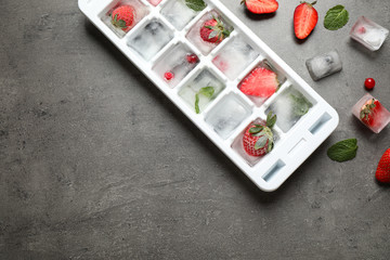 Obraz na płótnie Canvas Ice cubes with berries and tray on grey table, flat lay