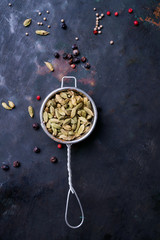 Green cardamom pods heap in a strainer over rustic metal background. Top view