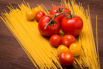 Ripe tomatoes and cherry on spaghetti on a wooden background