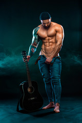 Fototapeta na wymiar Strong and fit man bodybuilder with guitrar shows abdominal muscles. Sporty muscular guy athlete. Sport and fitness concept. Men's fashion.
