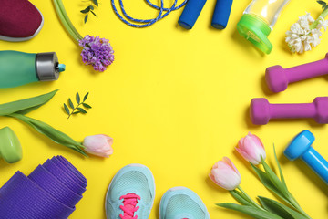 Frame made with spring flowers and sports items on yellow background, flat lay. Space for text