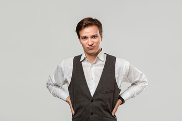 Young man in a white shirt and grey vest in high dudgeon over grey background