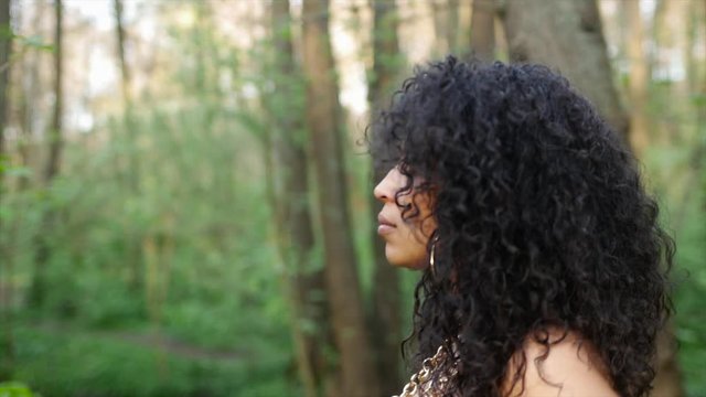 Black woman with curly hair is walking through a forrest. Slow Motion. Model is the singer and vocalist Marlene Johnson, Side View