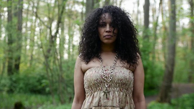 Black woman with curly hair is walking through a forrest. Slow Motion. Model is the singer and vocalist Marlene Johnson, Front View