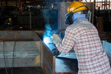 The welder is welding a steel structure work with process Flux Cored Arc Welding(FCAW) and dressed properly with personal protective equipment(PPE) for safety, at industrial factory.