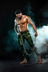 Athlete bodybuilder on black background with lights and smoke. Men fashion. Portrait of a brutal bearded man topless with chains.