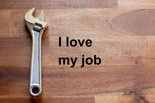 a flexible chromed adjustable wrench lies on a dark wooden table. The solgan I love my job is written on the table in black letters